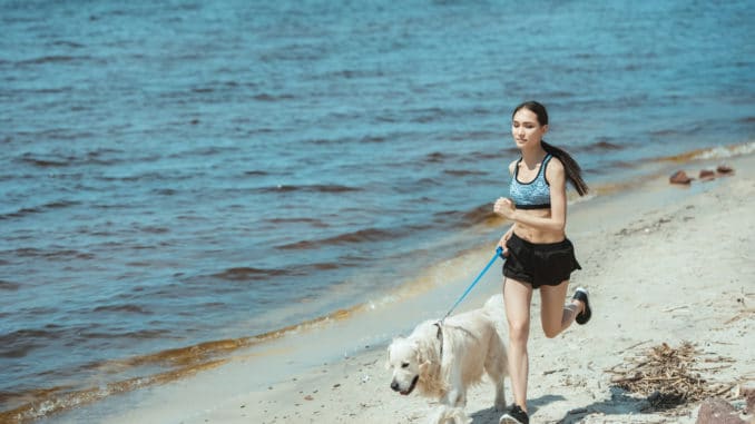 Frau joggt mit Hund am Strand